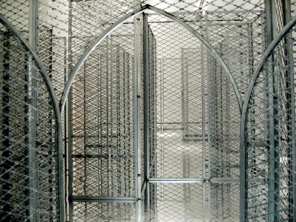 Akropolis Now, Kendell Geers, 2004. Visto aquí. La obra consiste en 18 paneles verticales de malla de alambre con concertinas en posición vertical y en el interior de una estructura modular metálica. | Fuente: http://lamiradapaseante.blogspot.com/2013/11/akropolis-now-concertinas.html