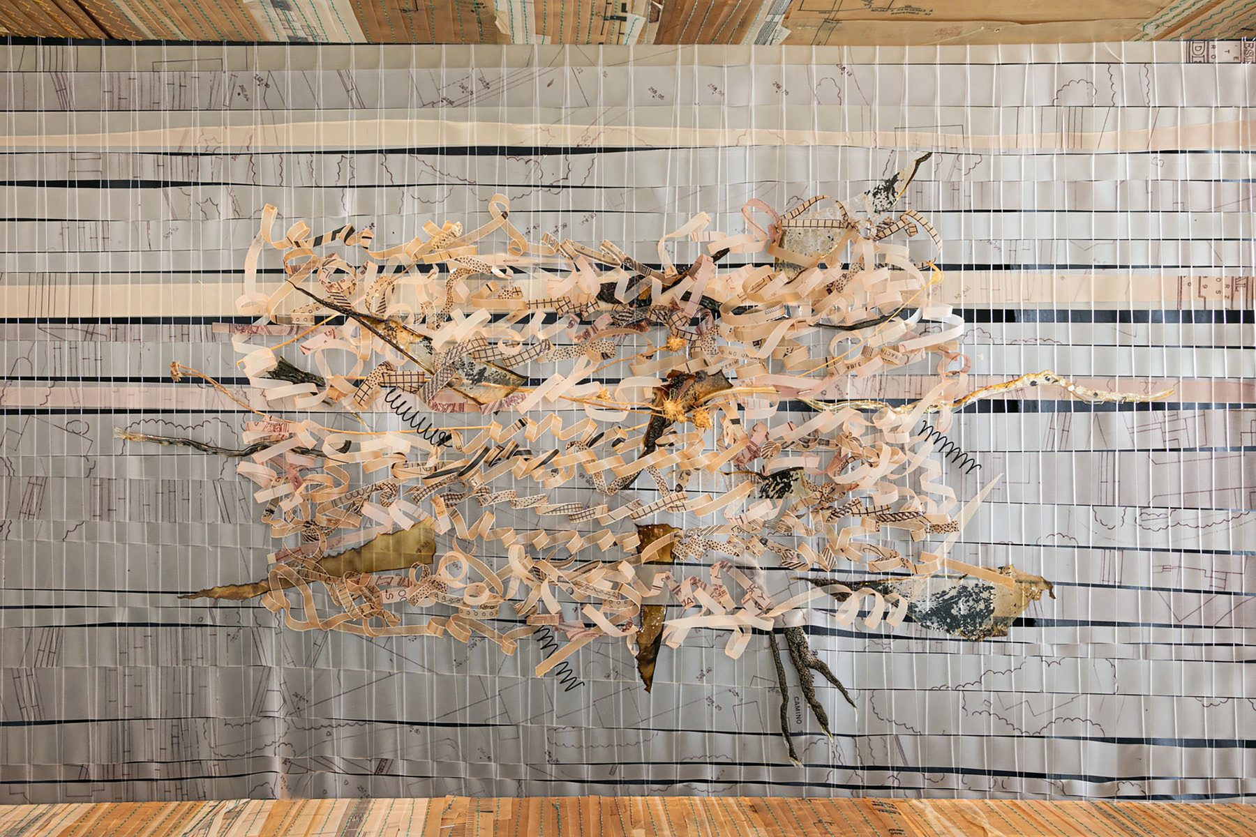 Loom-woven piece with a warp of black-and-white strips of plans, with a tangle of paper fragments, twigs and dry leaves gathered in the centre.