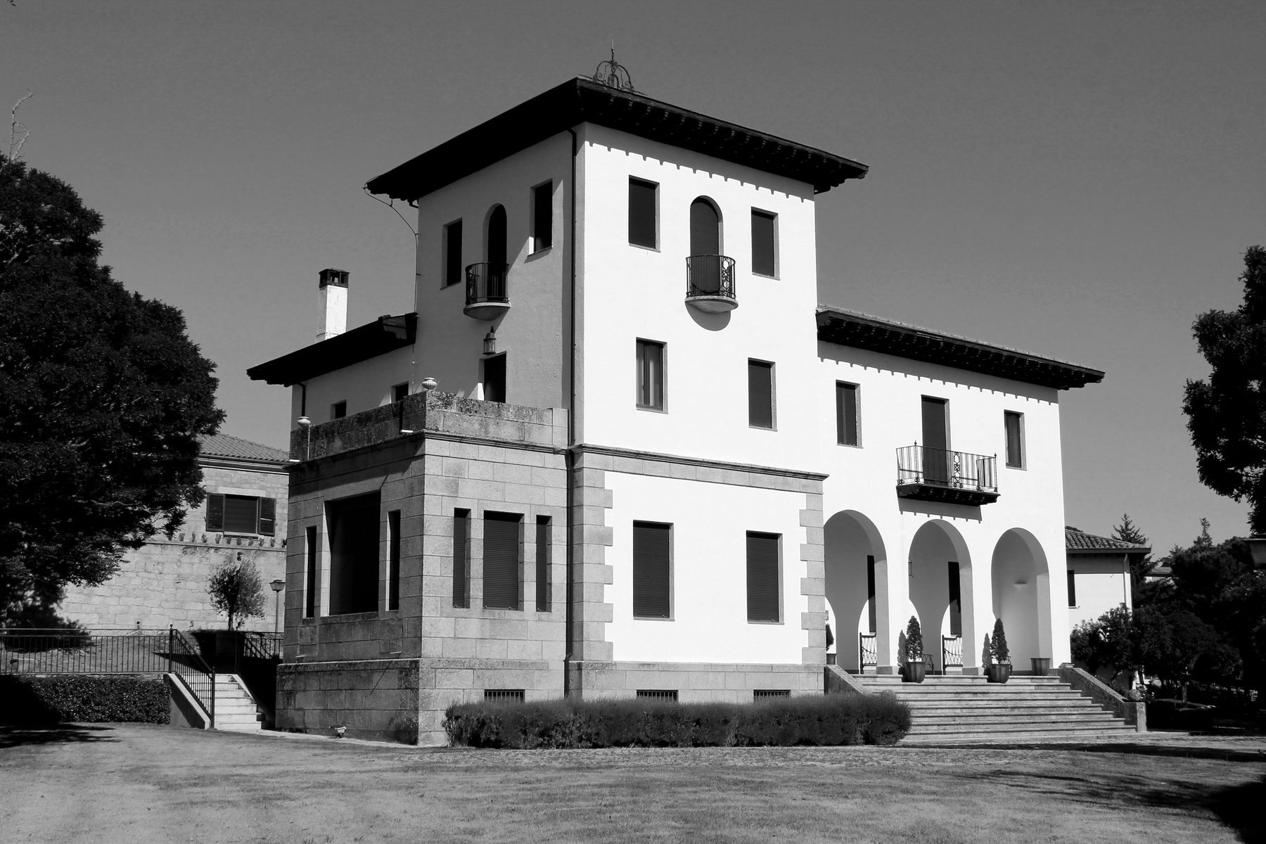 Fotografía en blanco y negro del hotel-dirección: casa de dos plantas con torreón de tres alturas, aleros pronunciados, zócalo de sillería, porche de tres arcos y escalinata de acceso.